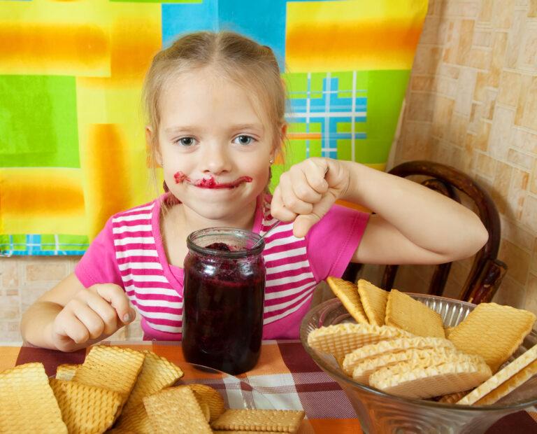 Little girl eating jam from  jar at kitchen